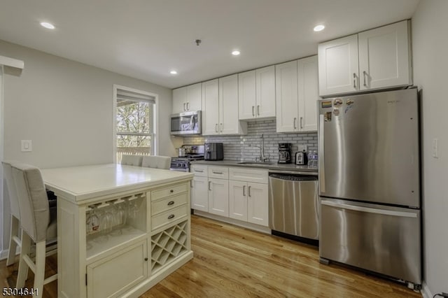 kitchen featuring white cabinetry, stainless steel appliances, sink, light hardwood / wood-style flooring, and backsplash