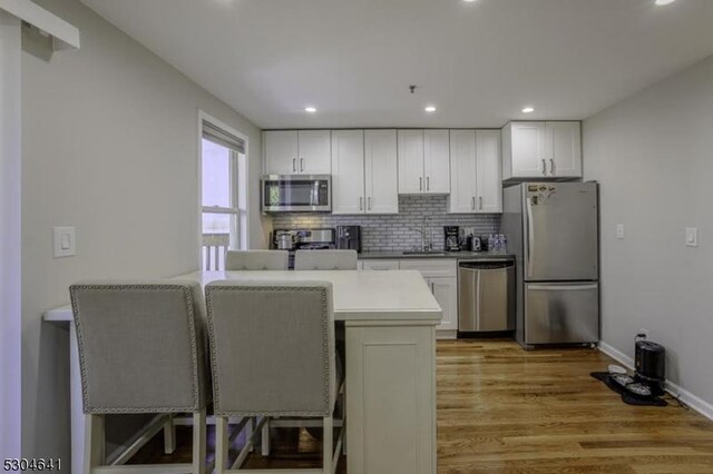 kitchen featuring stainless steel appliances, white cabinets, sink, backsplash, and light wood-type flooring