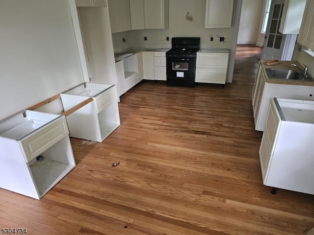 kitchen with hardwood / wood-style floors, sink, black stove, and white cabinetry