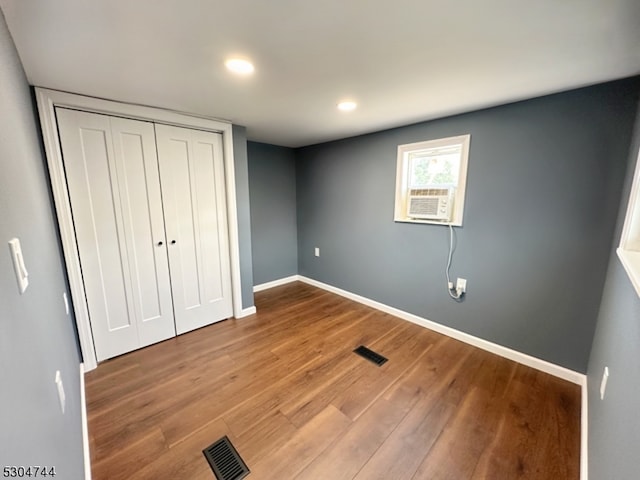 unfurnished bedroom featuring a closet, wood-type flooring, and cooling unit