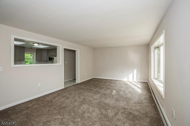 empty room with carpet floors, a baseboard radiator, a wealth of natural light, and baseboards