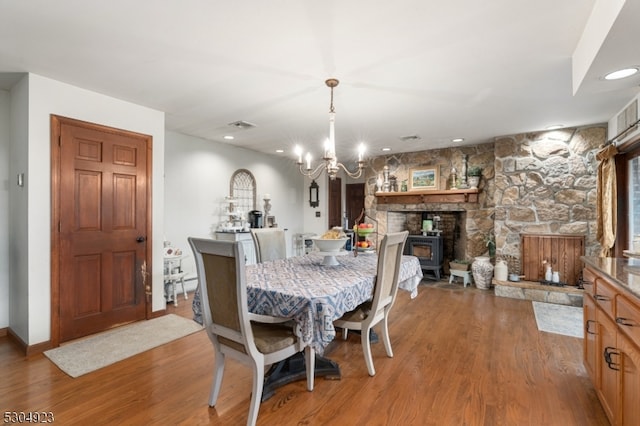 dining space featuring a stone fireplace, light hardwood / wood-style floors, a wood stove, and a notable chandelier