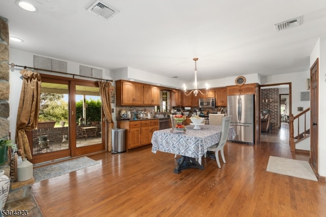 kitchen featuring hardwood / wood-style flooring, an inviting chandelier, backsplash, appliances with stainless steel finishes, and decorative light fixtures