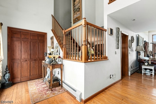 interior space featuring wood-type flooring, baseboard heating, and a high ceiling