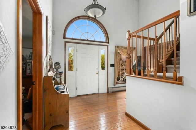 entrance foyer featuring a baseboard radiator, wood-type flooring, and a towering ceiling