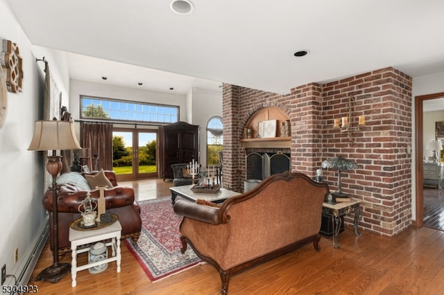 living room with hardwood / wood-style flooring, baseboard heating, french doors, and a brick fireplace