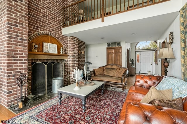 living room with wood-type flooring, a fireplace, a towering ceiling, and brick wall