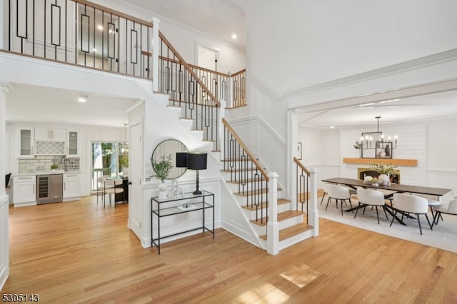 stairway with beverage cooler, a notable chandelier, hardwood / wood-style flooring, and crown molding