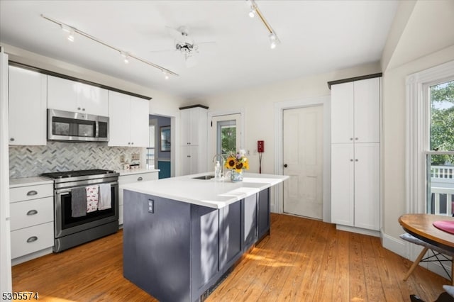 kitchen featuring light hardwood / wood-style floors, appliances with stainless steel finishes, tasteful backsplash, and an island with sink