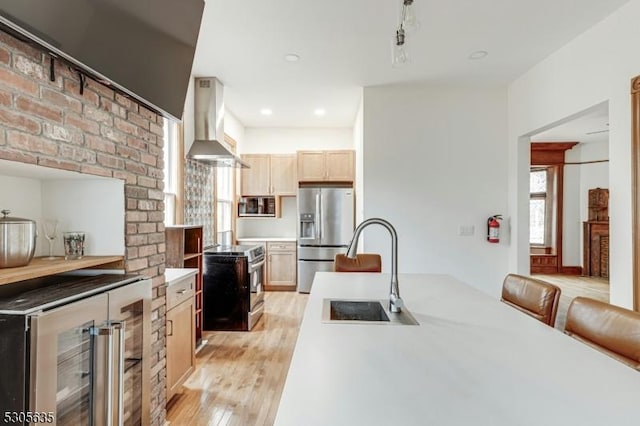 kitchen featuring wall chimney range hood, light wood-type flooring, light brown cabinetry, stainless steel appliances, and beverage cooler