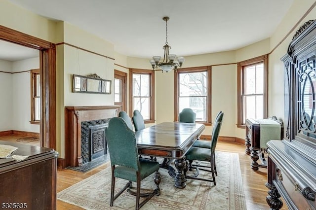 dining area with an inviting chandelier, a tiled fireplace, and light hardwood / wood-style flooring