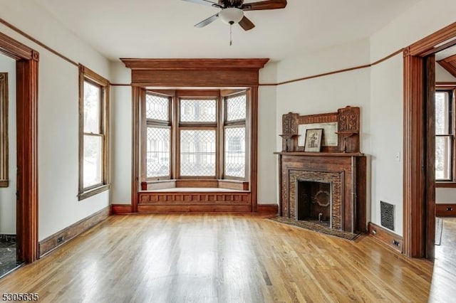 unfurnished living room featuring ceiling fan, a fireplace, and light wood-type flooring