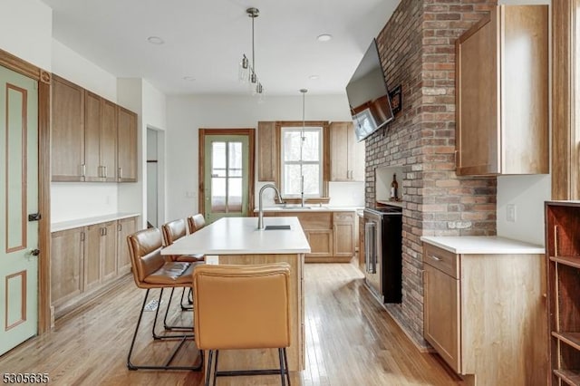 kitchen with a breakfast bar, sink, pendant lighting, a center island with sink, and light hardwood / wood-style flooring