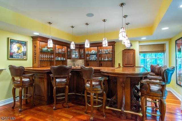 bar with dark hardwood / wood-style flooring, decorative light fixtures, tasteful backsplash, and a raised ceiling