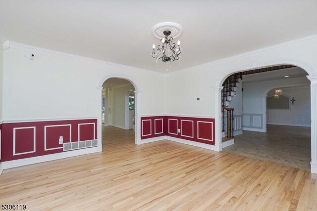 empty room with a notable chandelier, ornamental molding, and hardwood / wood-style floors