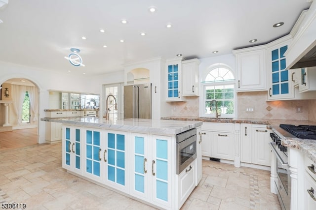 kitchen featuring decorative backsplash, white cabinetry, a center island with sink, light hardwood / wood-style floors, and high end appliances