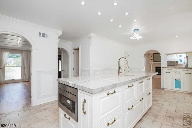 kitchen featuring an island with sink, oven, white cabinets, light hardwood / wood-style flooring, and sink