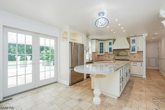 kitchen with an island with sink, white cabinetry, premium range hood, stainless steel fridge, and light tile patterned floors