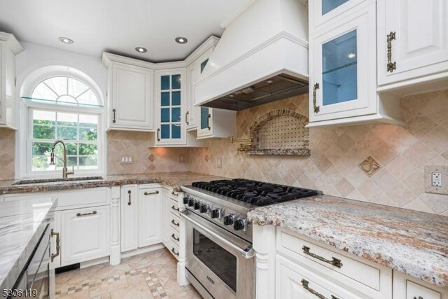 kitchen with decorative backsplash, custom exhaust hood, light tile patterned floors, sink, and stainless steel stove