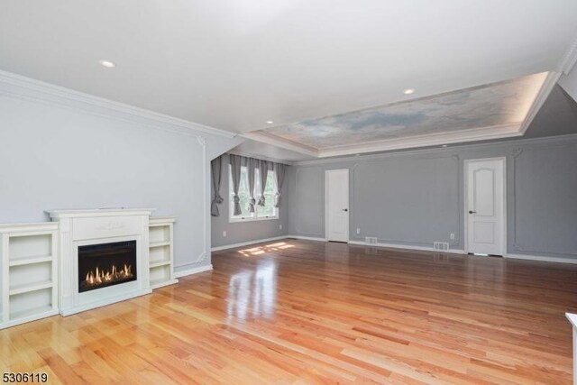 unfurnished living room with light wood-type flooring, crown molding, and a tray ceiling