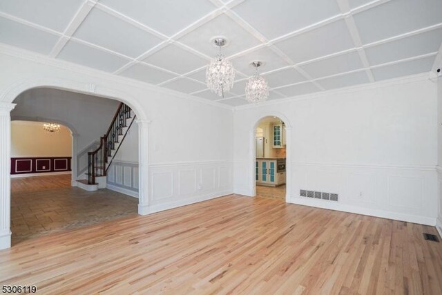 empty room featuring a notable chandelier, light wood-type flooring, and coffered ceiling