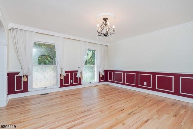 spare room with light wood-type flooring, ornamental molding, and a chandelier