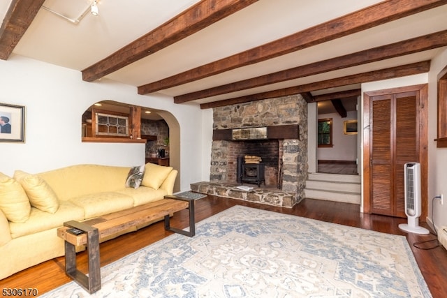 living room featuring beam ceiling, dark hardwood / wood-style floors, and a stone fireplace