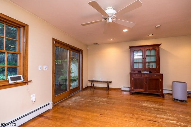 interior space featuring ceiling fan, light hardwood / wood-style floors, baseboard heating, and a healthy amount of sunlight