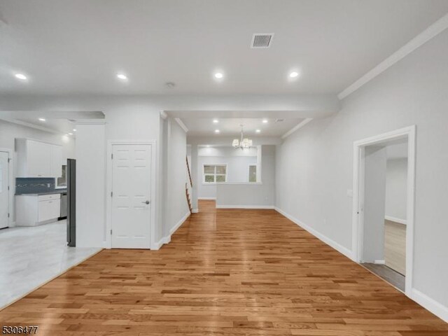 unfurnished living room featuring light wood-type flooring, crown molding, and a chandelier