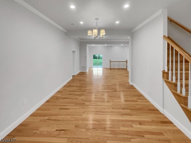 hall featuring light wood-type flooring, ornamental molding, and an inviting chandelier