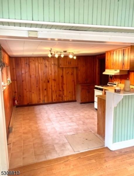 kitchen with light tile patterned flooring, wooden walls, track lighting, and exhaust hood