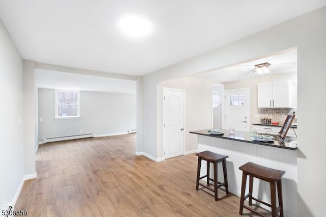 kitchen with white cabinetry, a baseboard radiator, kitchen peninsula, light hardwood / wood-style floors, and decorative backsplash