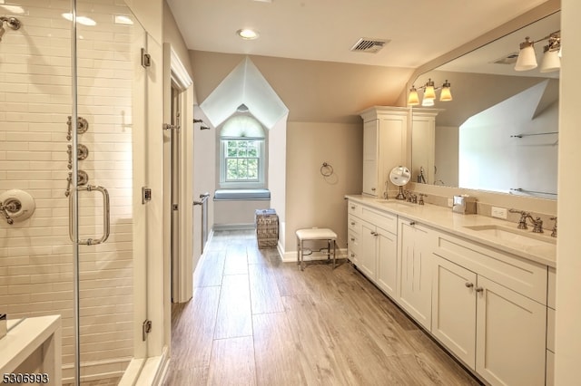 bathroom with wood-type flooring, vanity, vaulted ceiling, and a shower with door