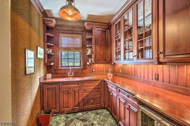 kitchen featuring pendant lighting, wooden walls, crown molding, and sink