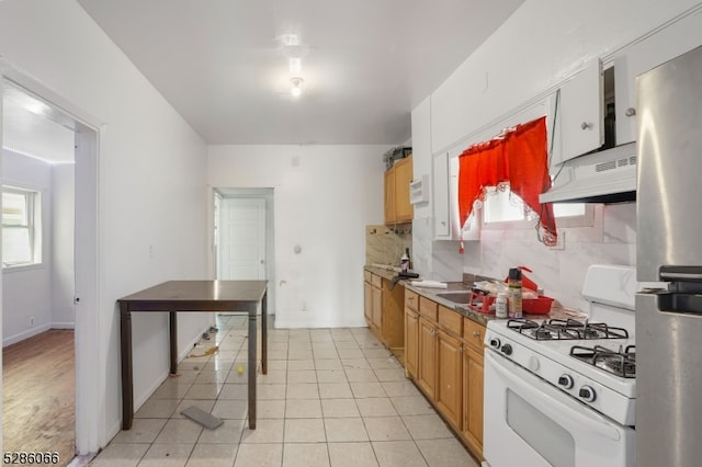 kitchen featuring backsplash, light tile patterned flooring, white range with gas cooktop, and stainless steel refrigerator