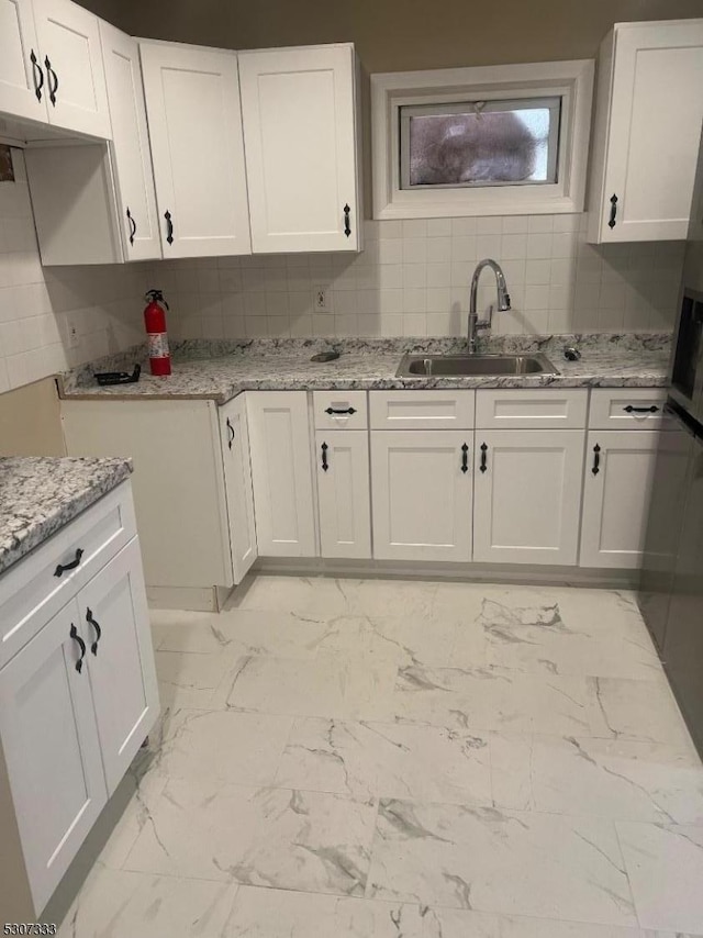 kitchen with light stone counters, sink, white cabinetry, and decorative backsplash