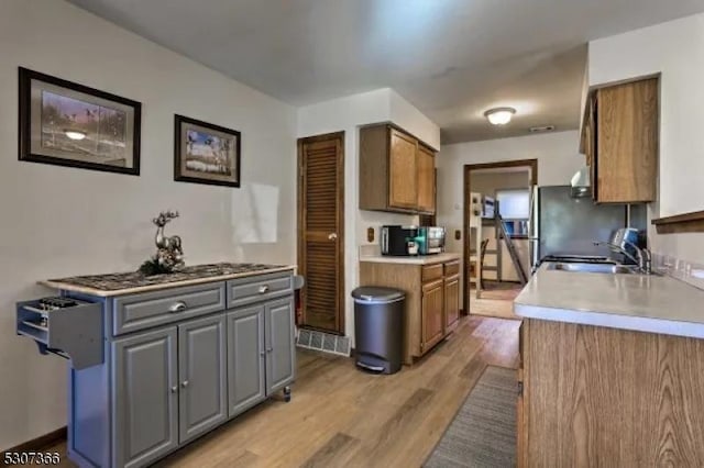 kitchen featuring light wood finished floors, stainless steel microwave, brown cabinets, gray cabinets, and a sink