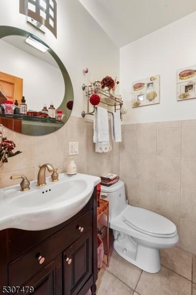 bathroom featuring toilet, tile patterned flooring, tasteful backsplash, vanity, and tile walls