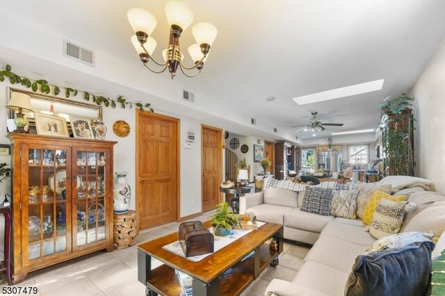 living room featuring a skylight, ceiling fan with notable chandelier, and light tile patterned floors