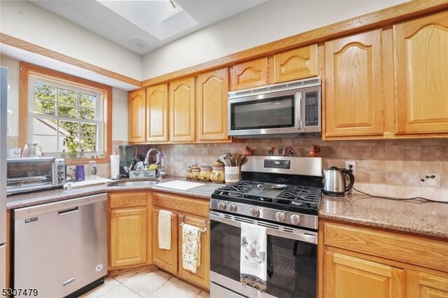 kitchen with sink, backsplash, light tile patterned flooring, and stainless steel appliances