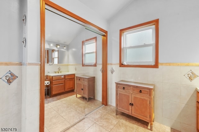 bathroom with decorative backsplash, tile patterned floors, vaulted ceiling, vanity, and tile walls