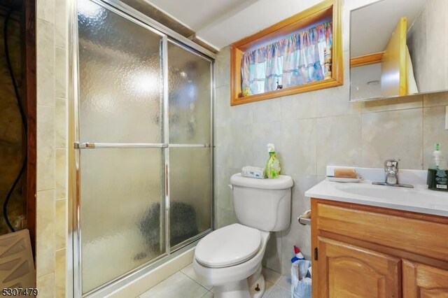 bathroom with toilet, vanity, tile walls, tile patterned floors, and a shower with shower door