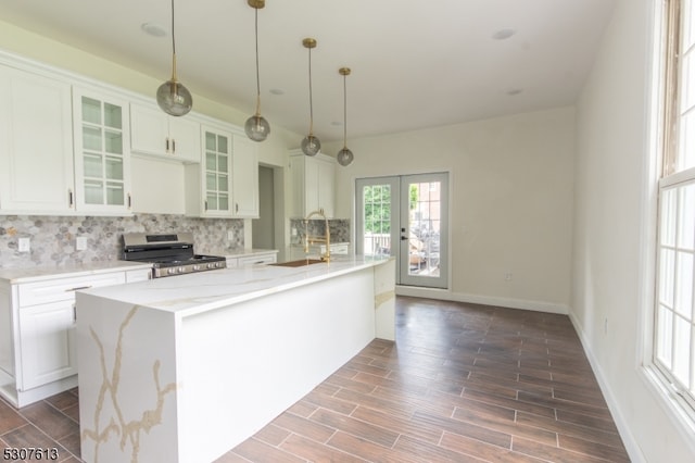 kitchen featuring a kitchen island with sink, dark wood-type flooring, stainless steel stove, white cabinets, and light stone counters