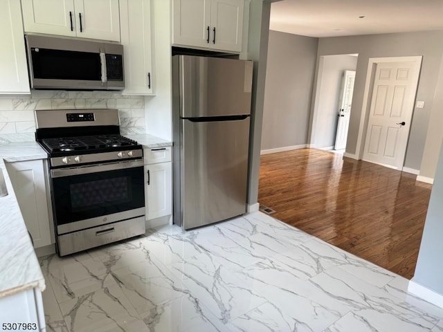 kitchen featuring appliances with stainless steel finishes, backsplash, white cabinetry, light stone counters, and light wood-type flooring