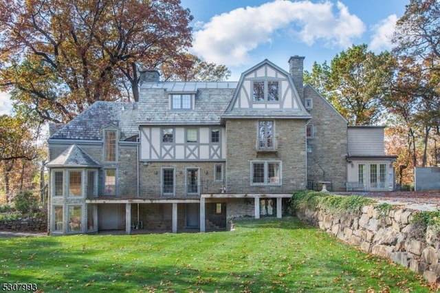 rear view of property featuring stone siding, a lawn, and a chimney