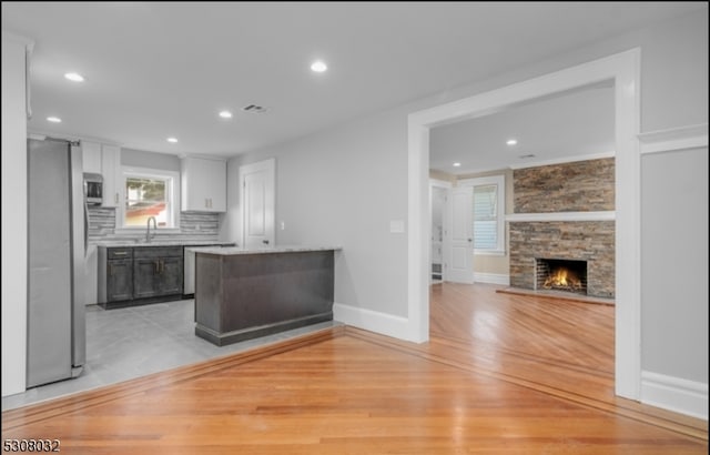 kitchen featuring backsplash, a stone fireplace, light hardwood / wood-style floors, stainless steel appliances, and white cabinets