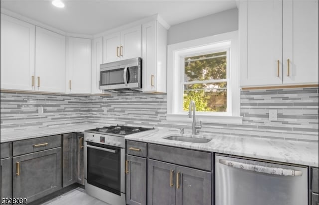 kitchen with tasteful backsplash, white cabinetry, appliances with stainless steel finishes, light stone countertops, and sink