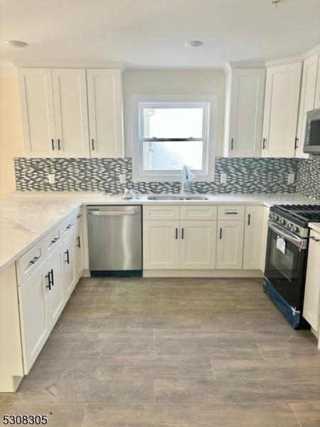 kitchen featuring tasteful backsplash, appliances with stainless steel finishes, white cabinetry, a sink, and light stone countertops