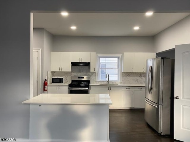 kitchen featuring stainless steel appliances, light countertops, a sink, a peninsula, and under cabinet range hood