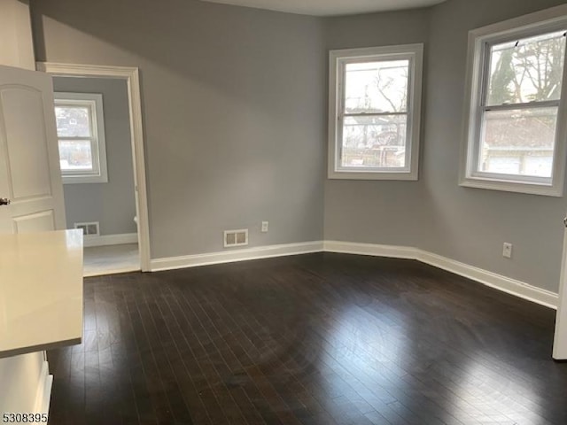 unfurnished room with dark wood-type flooring, a healthy amount of sunlight, and visible vents